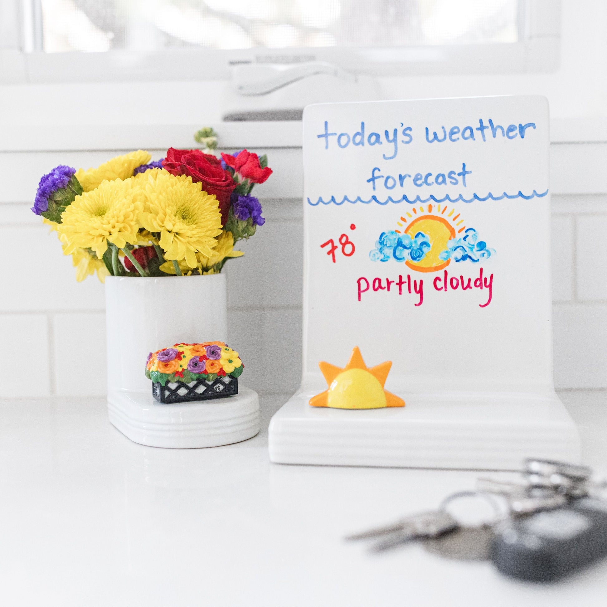 flower box mini on a cutie container filled with flowers, sunshine mini on a pinstripes message board with the weather report written on it and some car keys